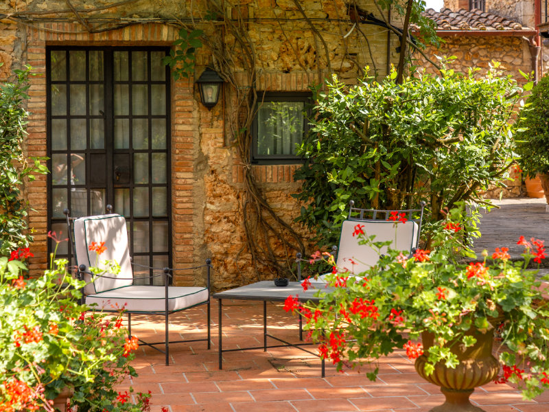 Cozy outdoor patio with cushioned chairs and a small table set against a rustic stone wall with a glass door and climbing vines